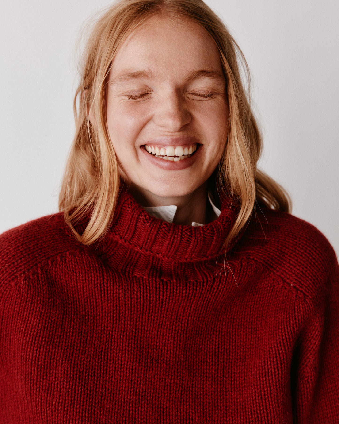 A model wearing a Bosie Blue Mogganer Womens Siren Merino Polo Neck Sweater in colour Russet Red.
