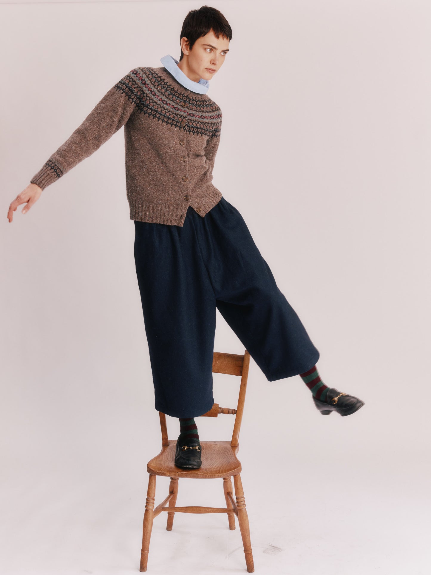 Woman wearing a Bosie Islander Cardigan and dark pants standing on a wooden stool against a plain background
