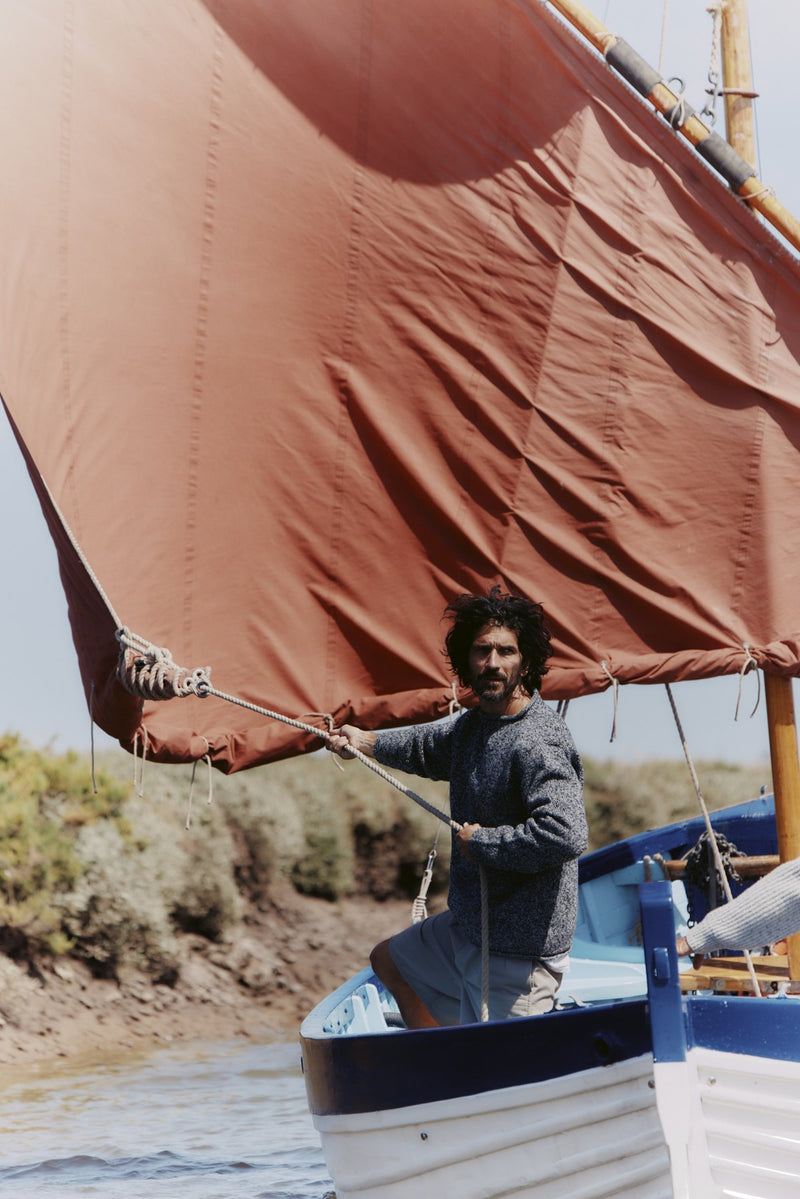 Fisherman holding the rope beneath a rust-red sail in a Bosie Blue Mogganer jumper – North Sea Knits