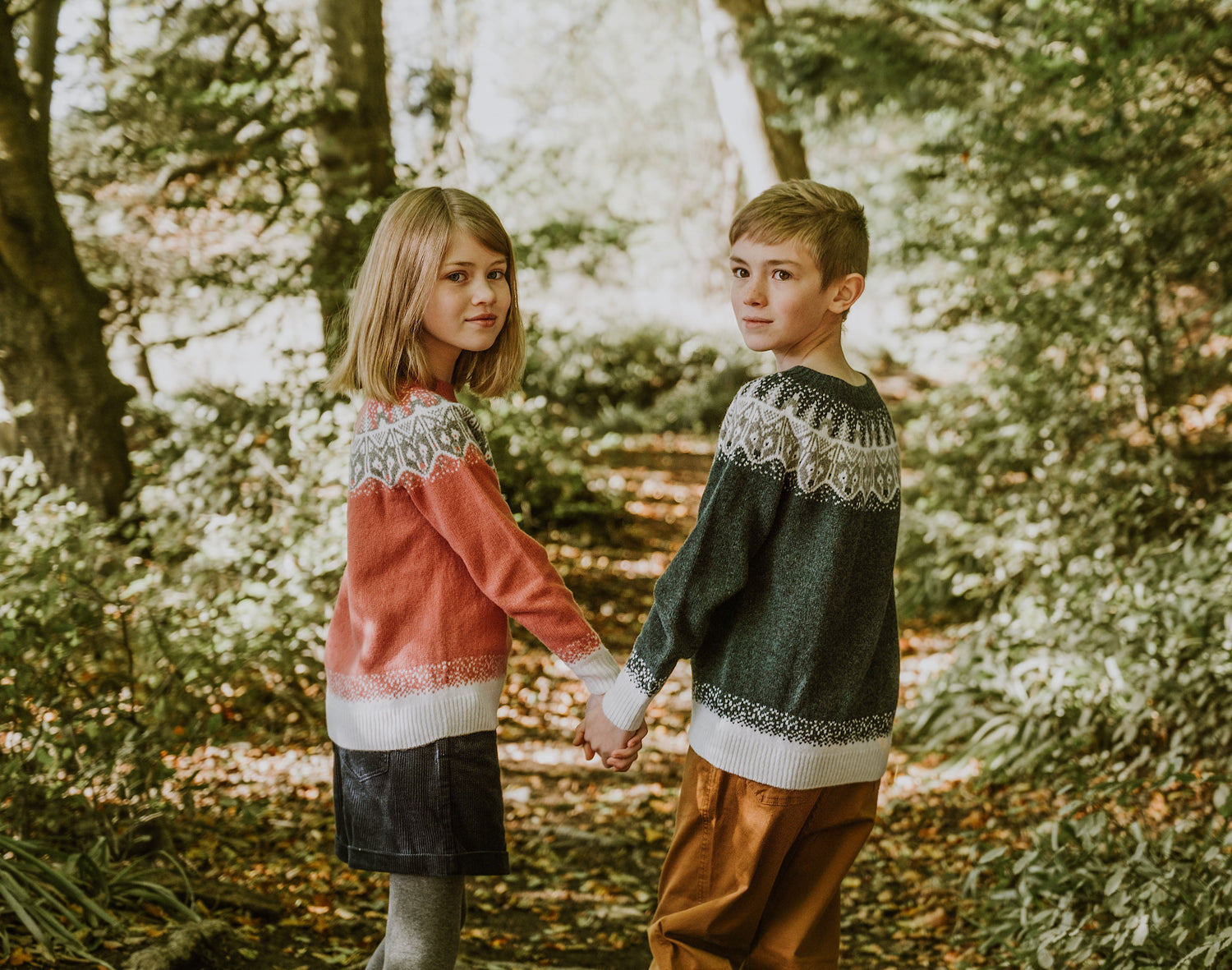 A girl and boy each in a Little Bosie Peter and the Wolf  sweater, holding hands.