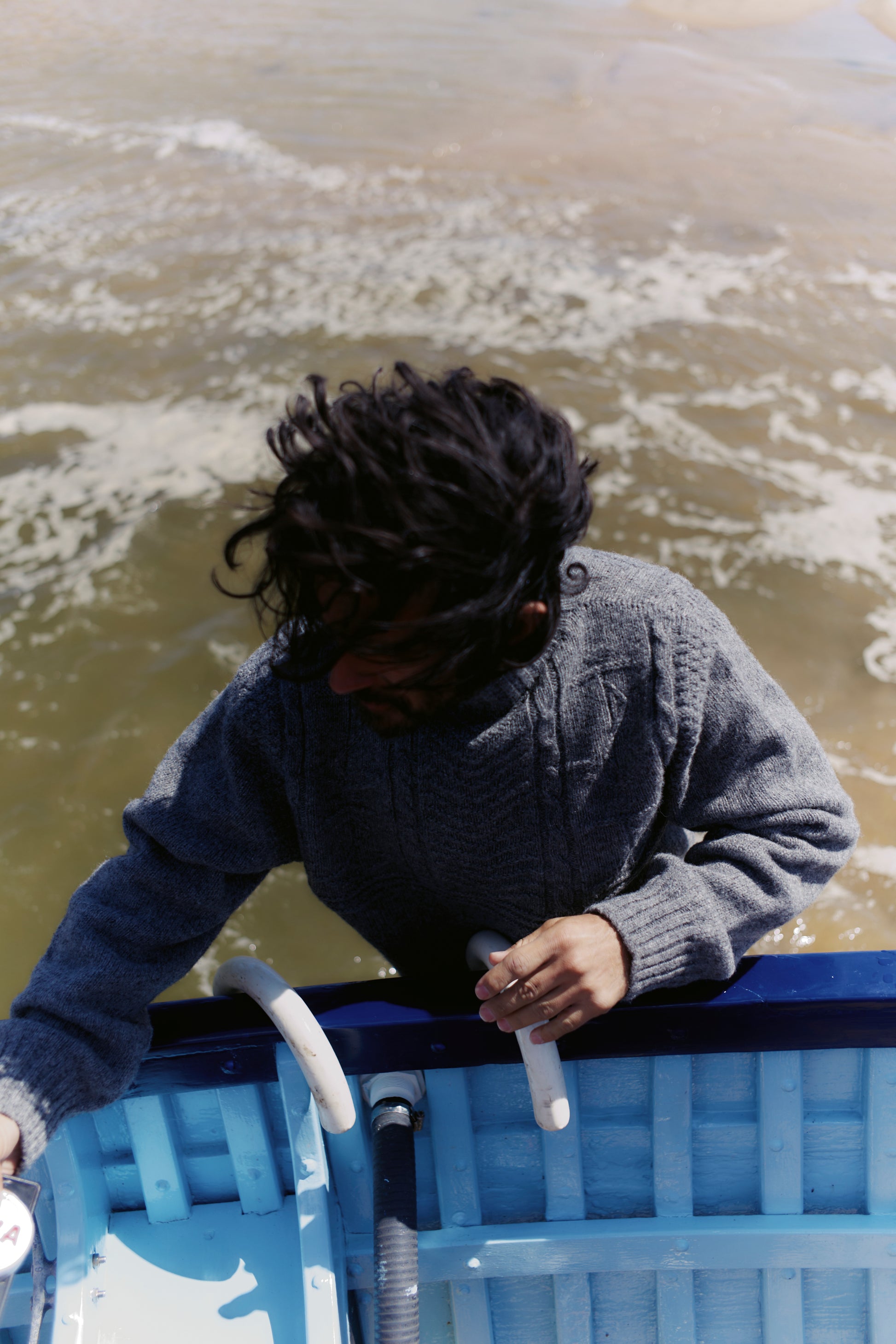 Person cleaning a blue boat by a body of water in a Bosie Ganjey.