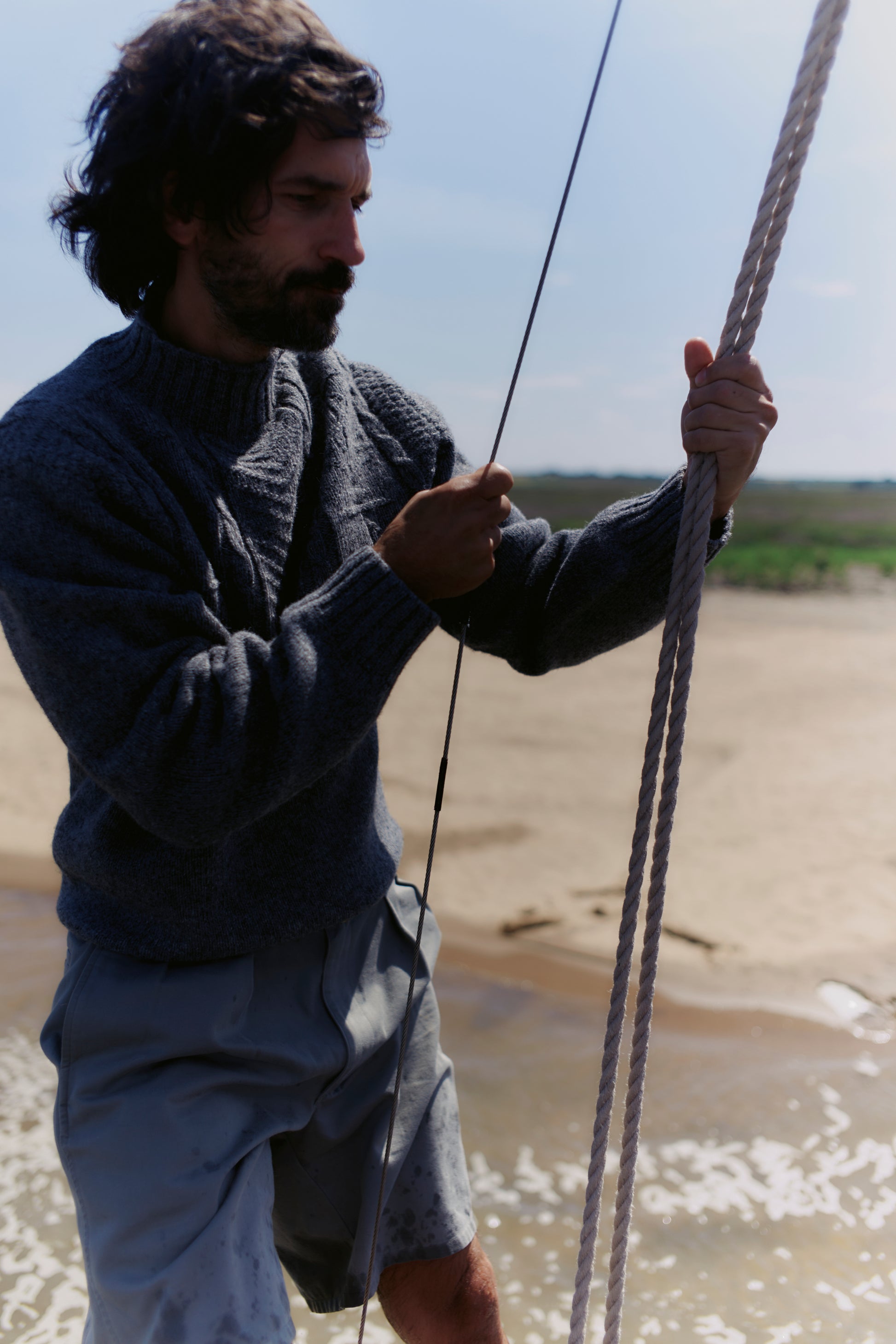 Man holding a rope by a body of water with a clear sky in a Bosie Ganjey