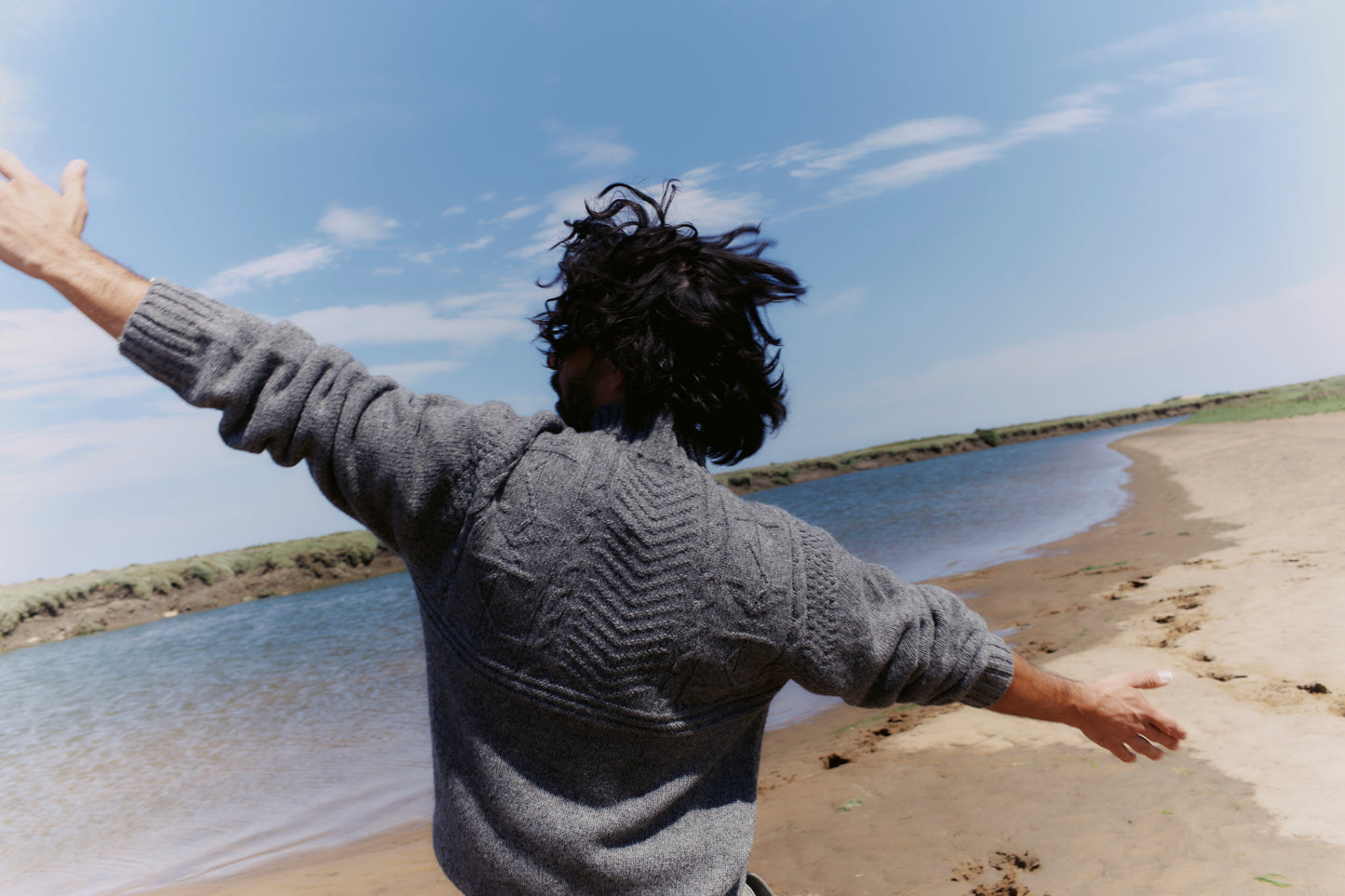 Person standing on a beach with arms outstretched, facing the ocean in a Bosie Ganjey.