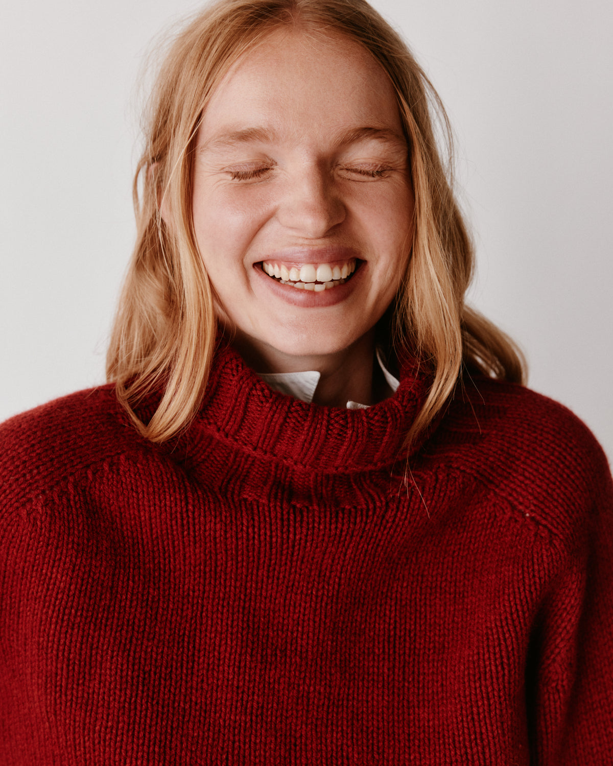 A model wearing a Bosie Blue Mogganer Womens Siren Merino Polo Neck Sweater in colour Russet Red.