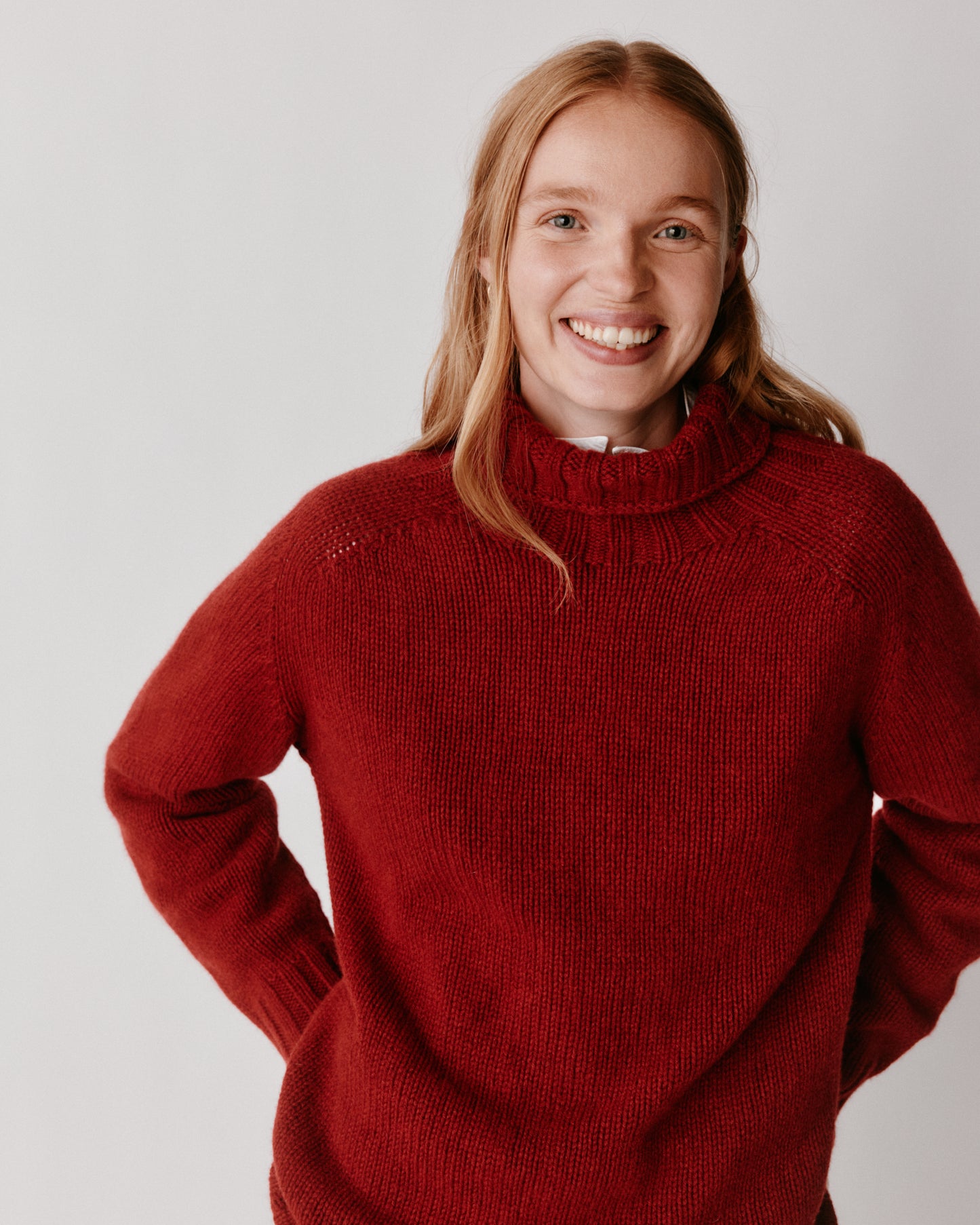 A model wearing a Bosie Blue Mogganer Womens Siren Merino Polo Neck Sweater in colour Russet Red.