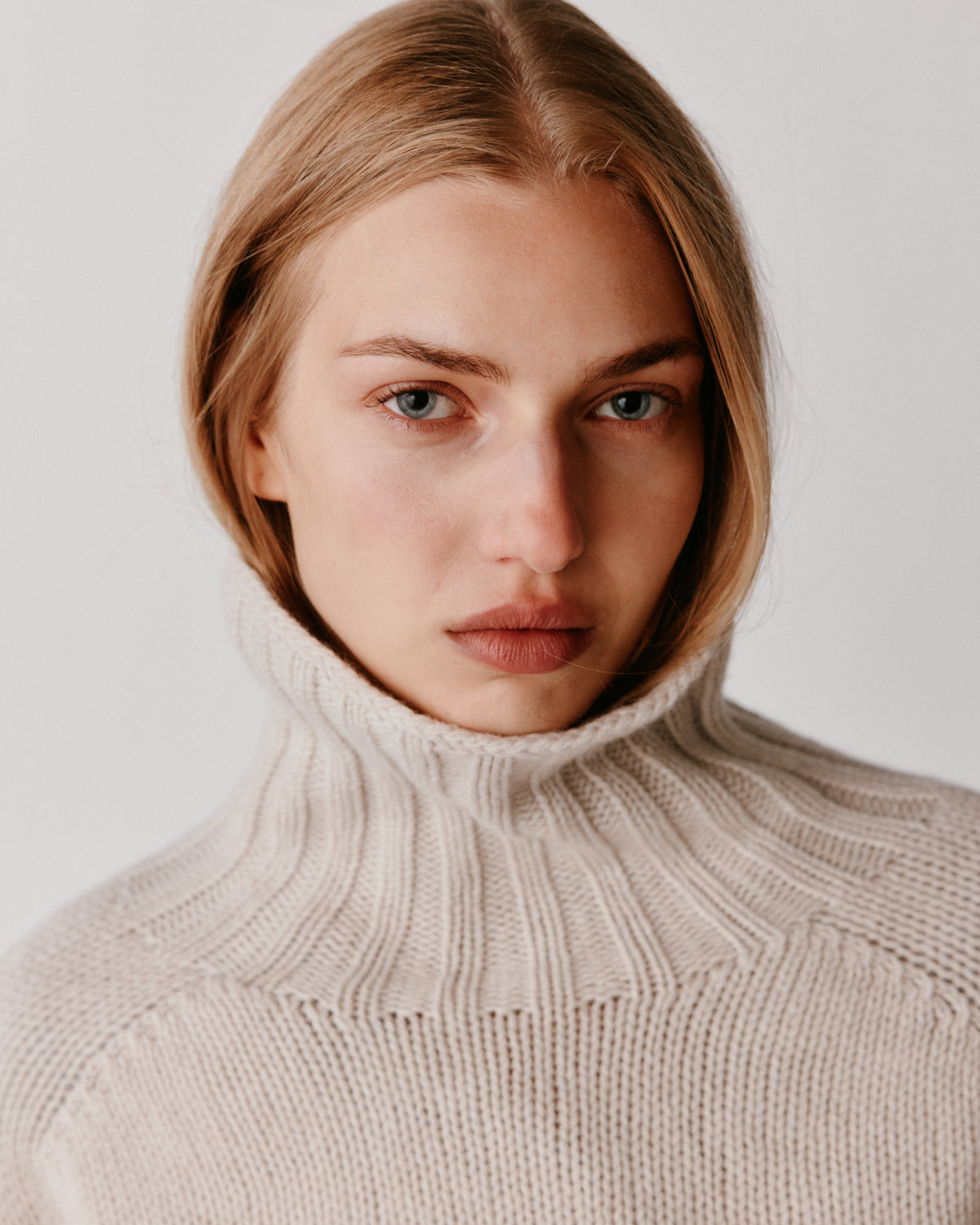 A model wearing a Bosie Blue Mogganer Womens Siren Merino Polo Neck Sweater in colour Swansdown.