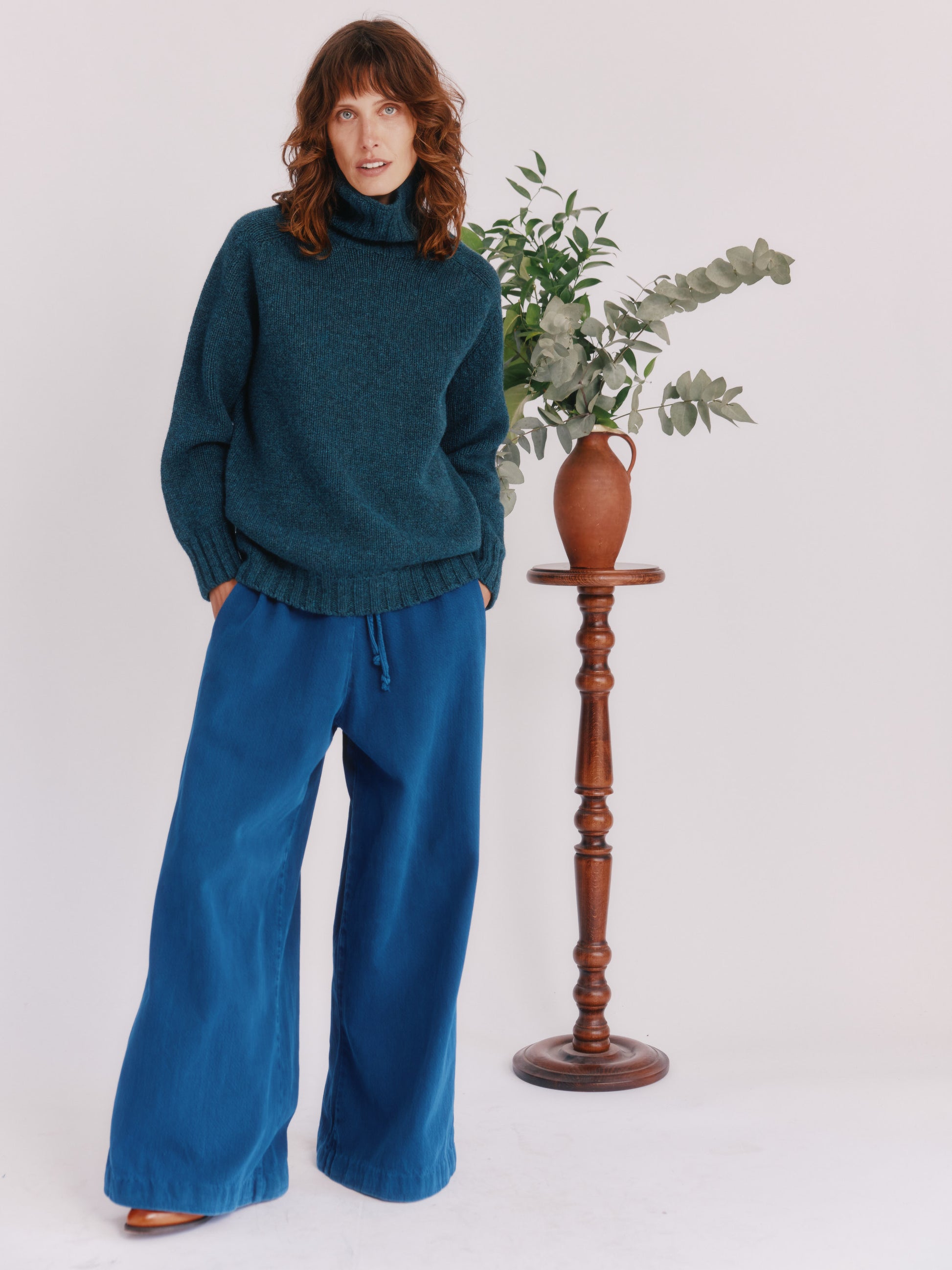 Model wearing a Bosie Knitwear Blue Mogganer Womens Siren Merino Polo Neck Sweater in colour Lugano Dark Teal.