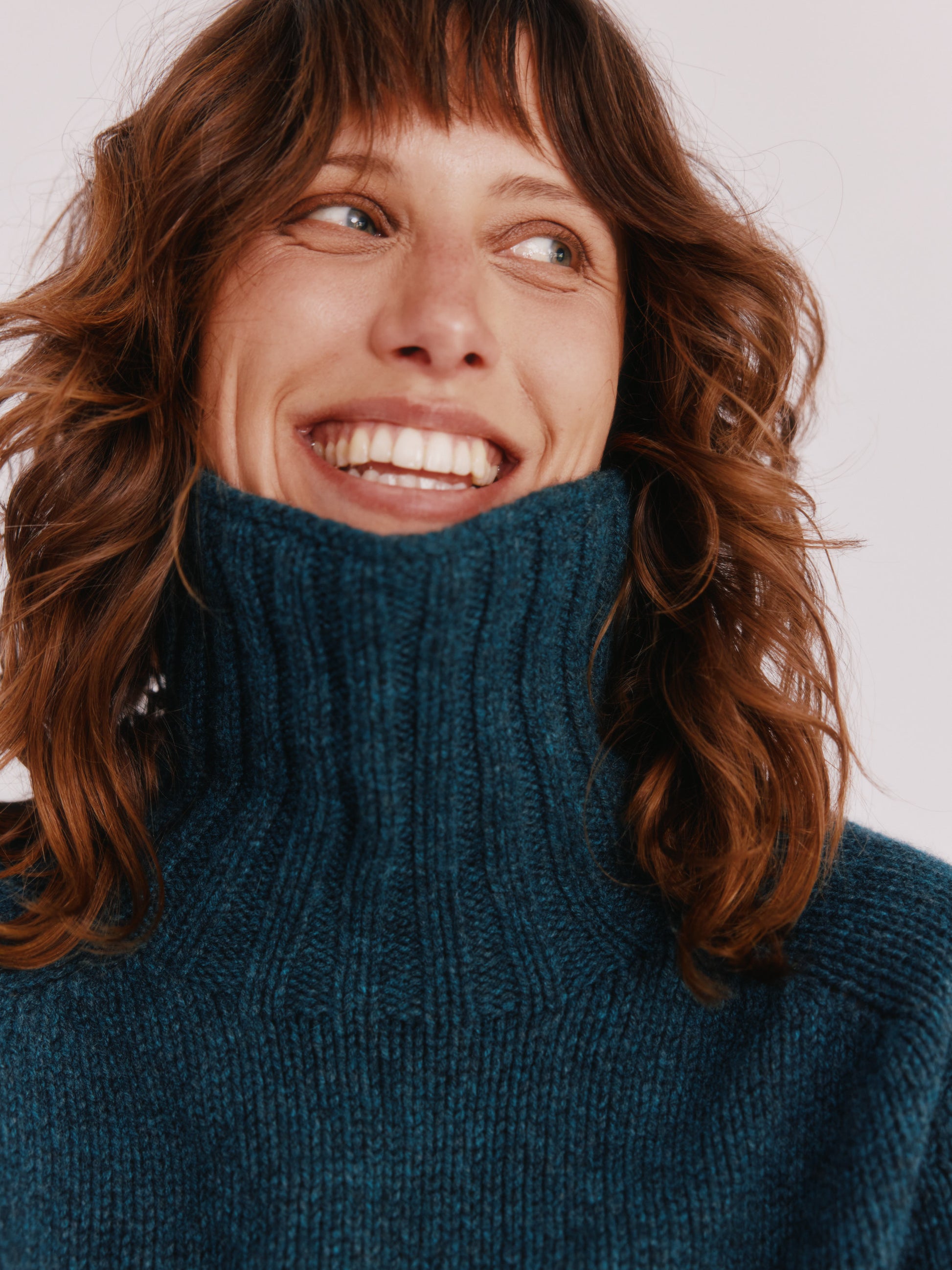 Model wearing a Bosie Knitwear Blue Mogganer Womens Siren Merino Polo Neck Sweater in colour Lugano Dark Teal.