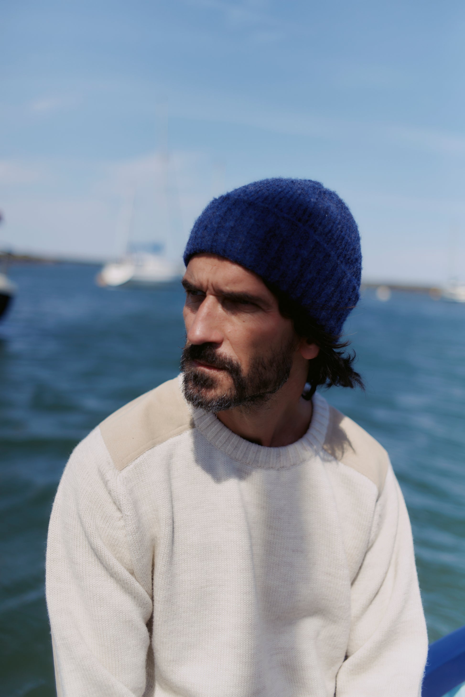 A Man wearing a Bosie Brushed Shetland Wool Beanie Hat Navy at Sea. 