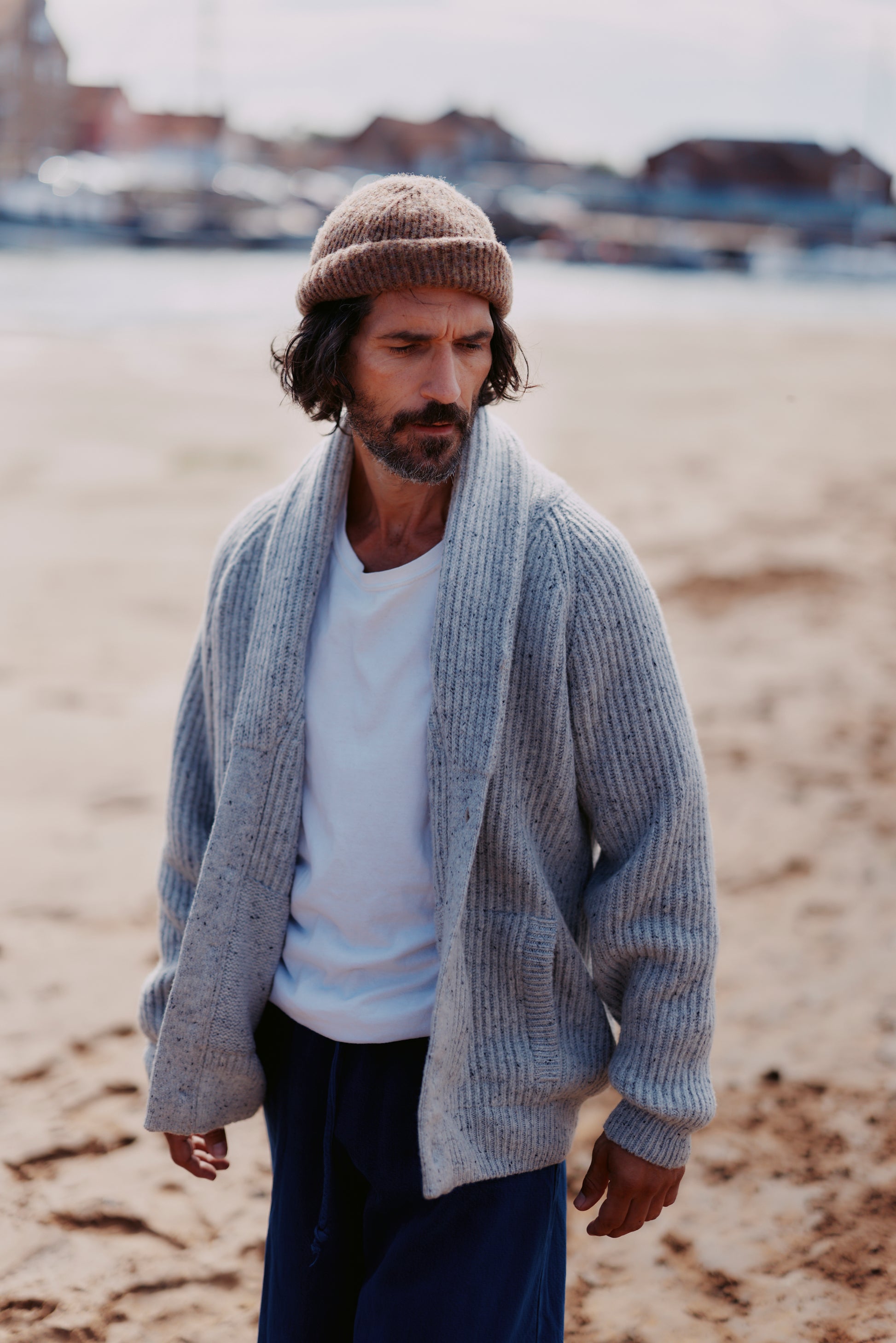 Man wearing a  Bosie Blue Mogganer Harbourmaster Cardigan and Heathland Brushed wool hat on a beach