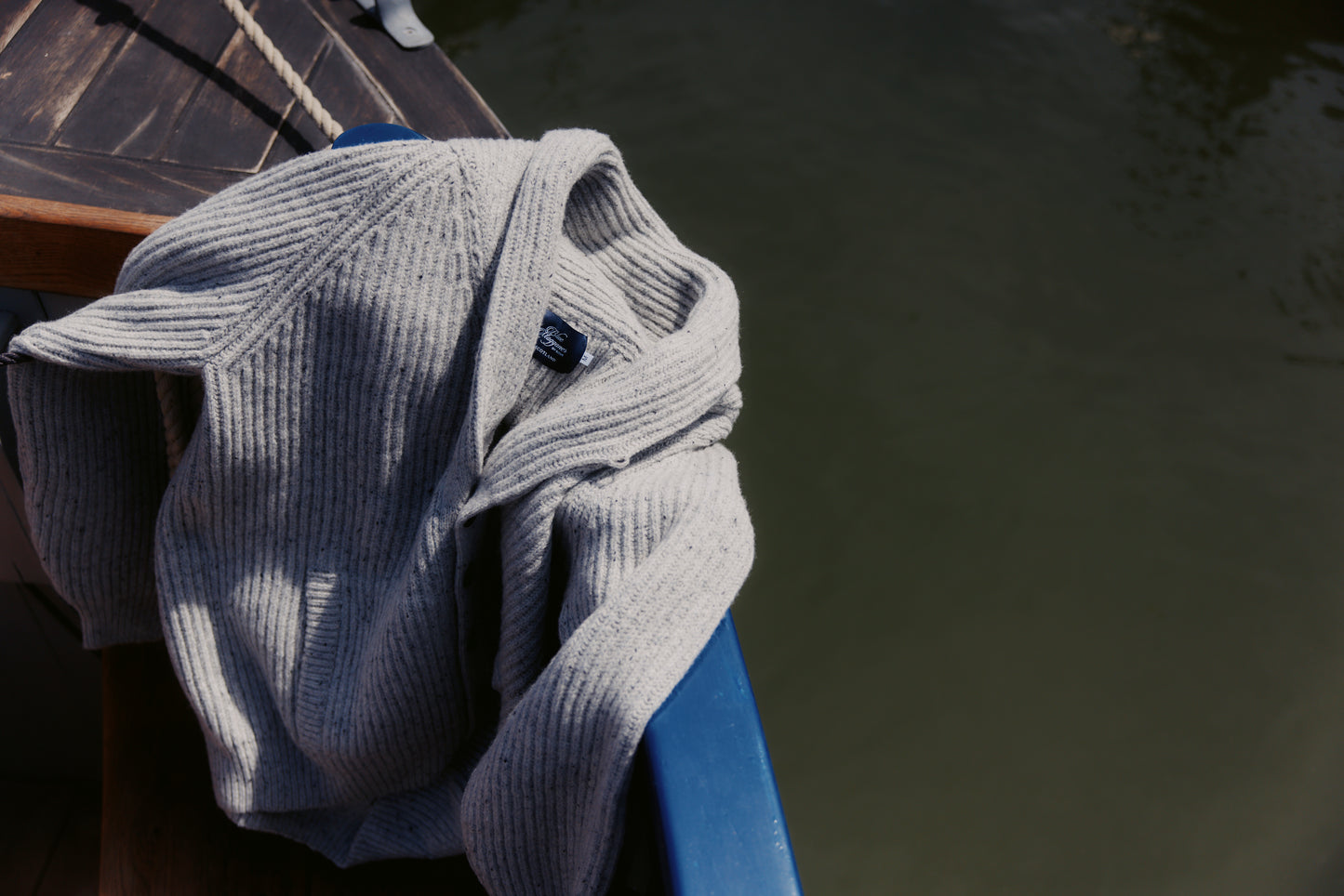  Bosie Blue Mogganer Harbourmaster Cardigan draped over a chair by a body of water