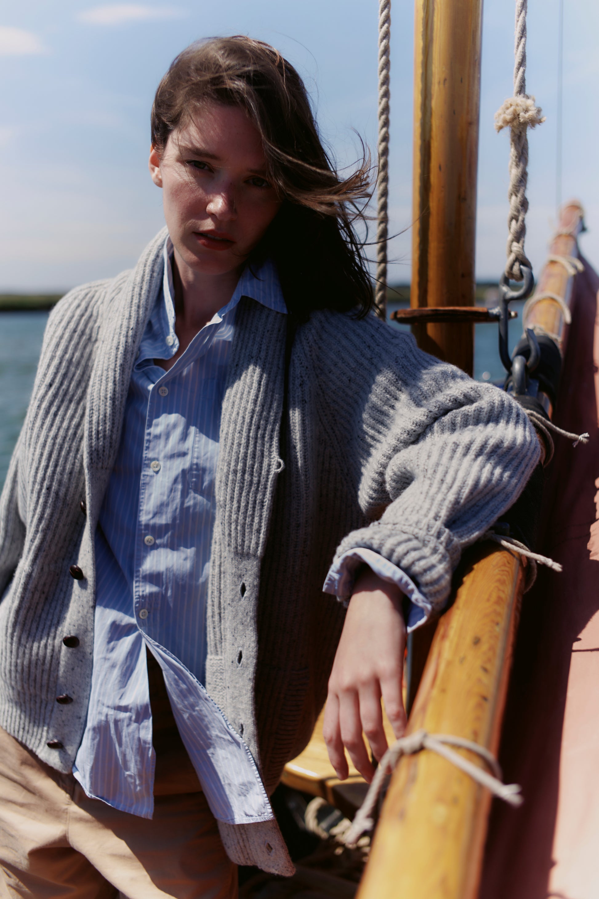Woman standing on a boat wearing a  Bosie Blue Mogganer Harbourmaster Cardigan and light blue shirt.