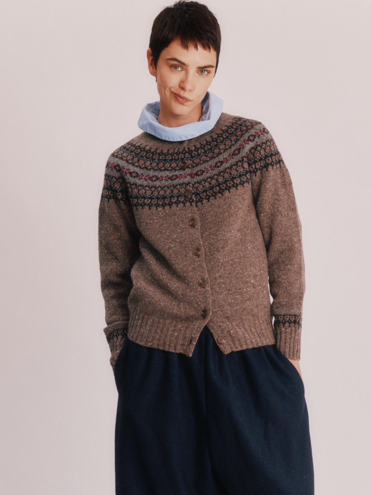 Woman wearing a Bosie Islander Cardigan and dark pants standing on a wooden stool against a plain background