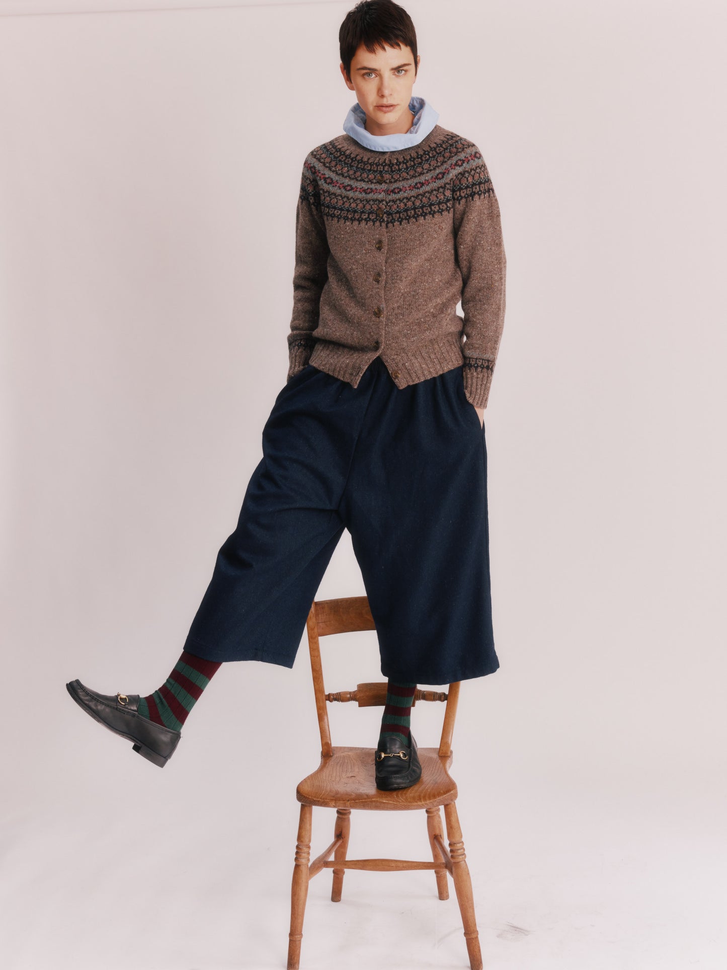 Woman wearing a Bosie Islander Cardigan and dark pants standing on a wooden stool against a plain background