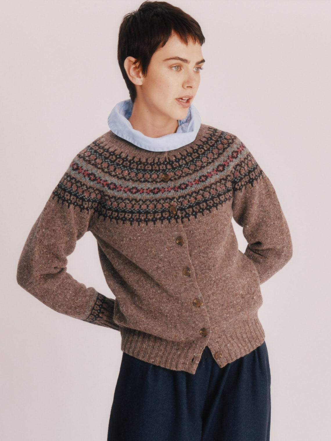 Woman wearing a Bosie Islander Cardigan and dark pants standing on a wooden stool against a plain background