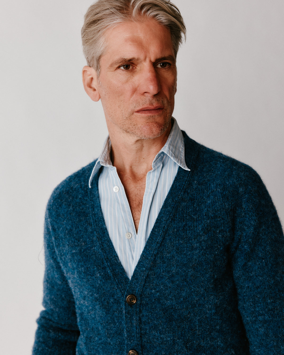 A model wearing a Bosie Harley of Scotland Shaggy Shetland Men's V Cardigan in colour Denim.