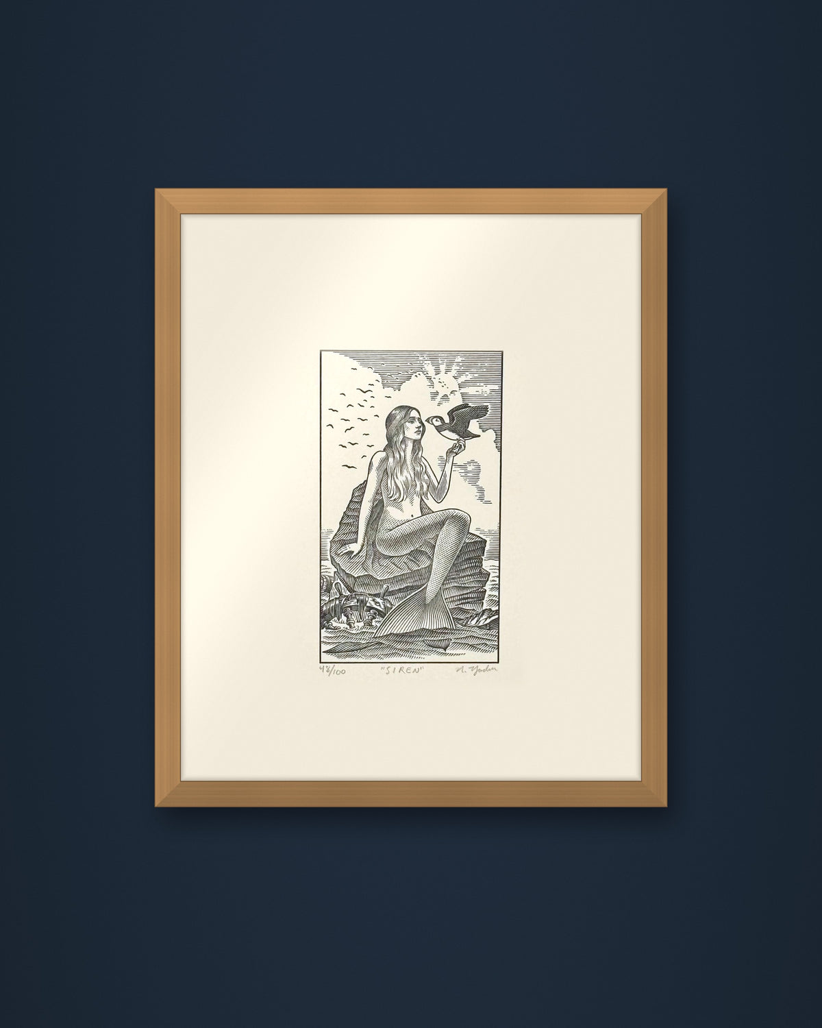 The Siren: hand-pressed, hand-signed limited edition print of Nathan Yoder's hand-drawn illustration for Bosie Knitwear's Blue Mogganer collection, shown in an oak frame on a navy wall (frame not included)