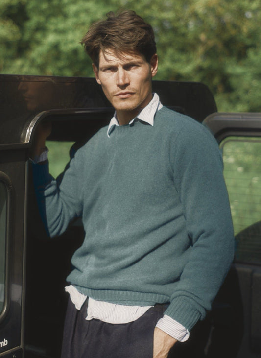 Man wearing the Bosie Harley of Scotland x Todd and Duncan Pure Men's Cashmere Sweater in Marine Blue beside a Land Rover – seamless, seam-free pure cashmere, knitted in Scotland by Harley of Scotland