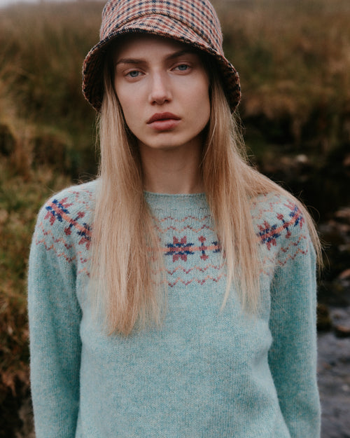 Woman wearing a Bosie Fair Isle yoke sweater in pale aqua with a houndstooth bucket hat on the Scottish moors – women's knitwear, made in Scotland