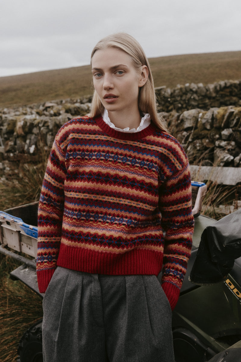Woman wearing a red allover Fair Isle jumper with a white frilled collar beside a drystone wall on the Scottish moors – Bosie women's knitwear, made in Scotland