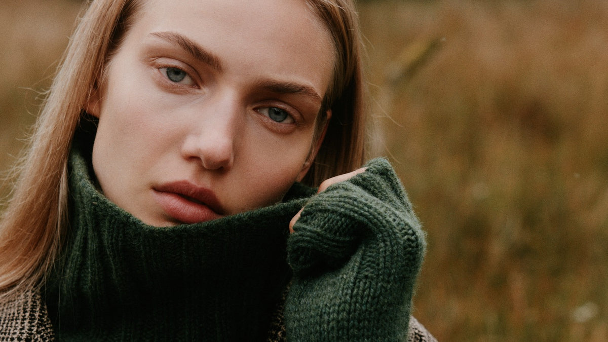 Woman in a green chunky roll neck jumper pulling the collar up to her face in autumn grass – Bosie Knitwear yarns, knitted in Scotland