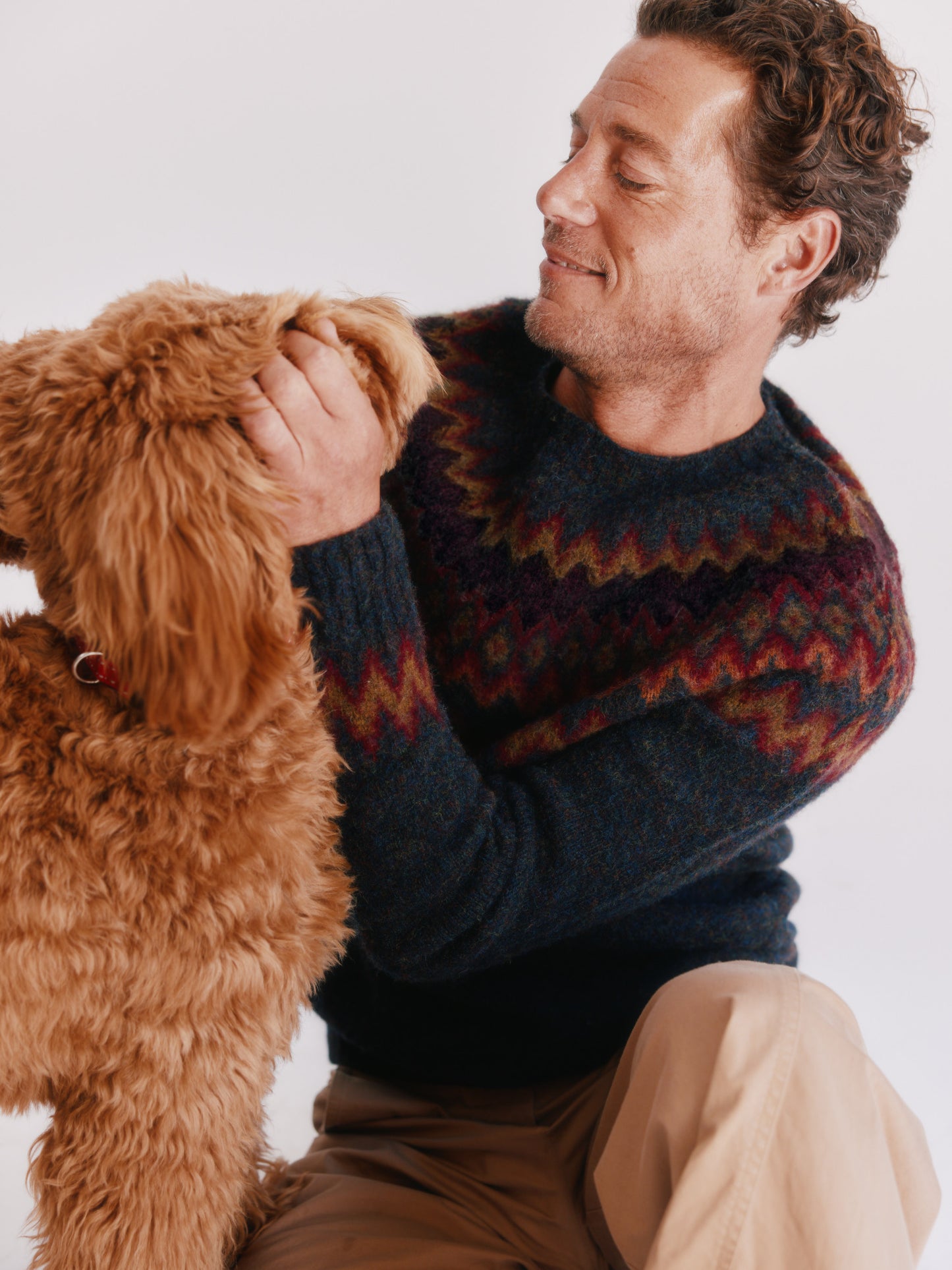 Man wearing a Bosie Fjord Nordic patterned sweater and beige pants on a white background