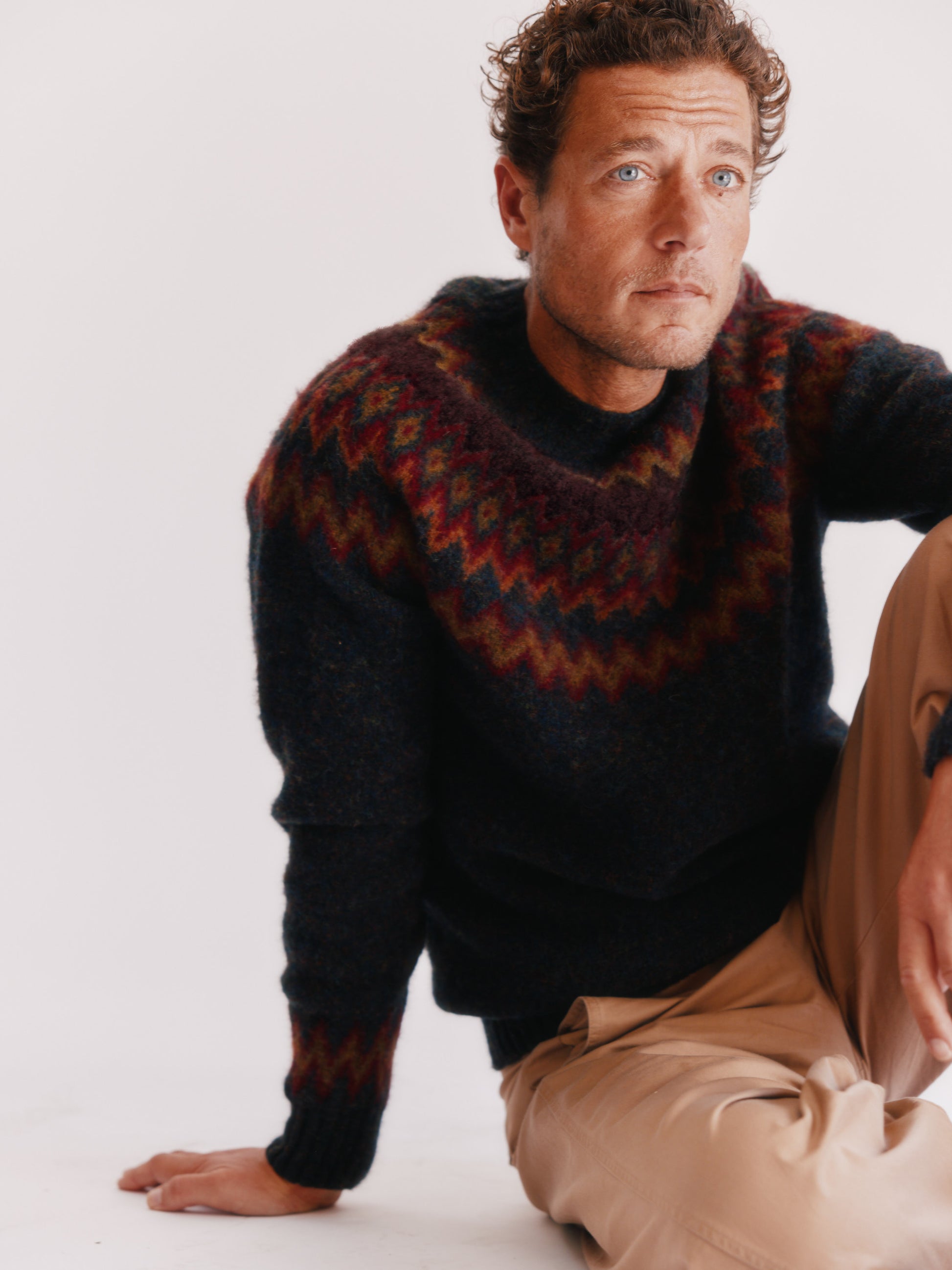 Man wearing a Bosie Fjord Nordic patterned sweater and beige pants on a white background