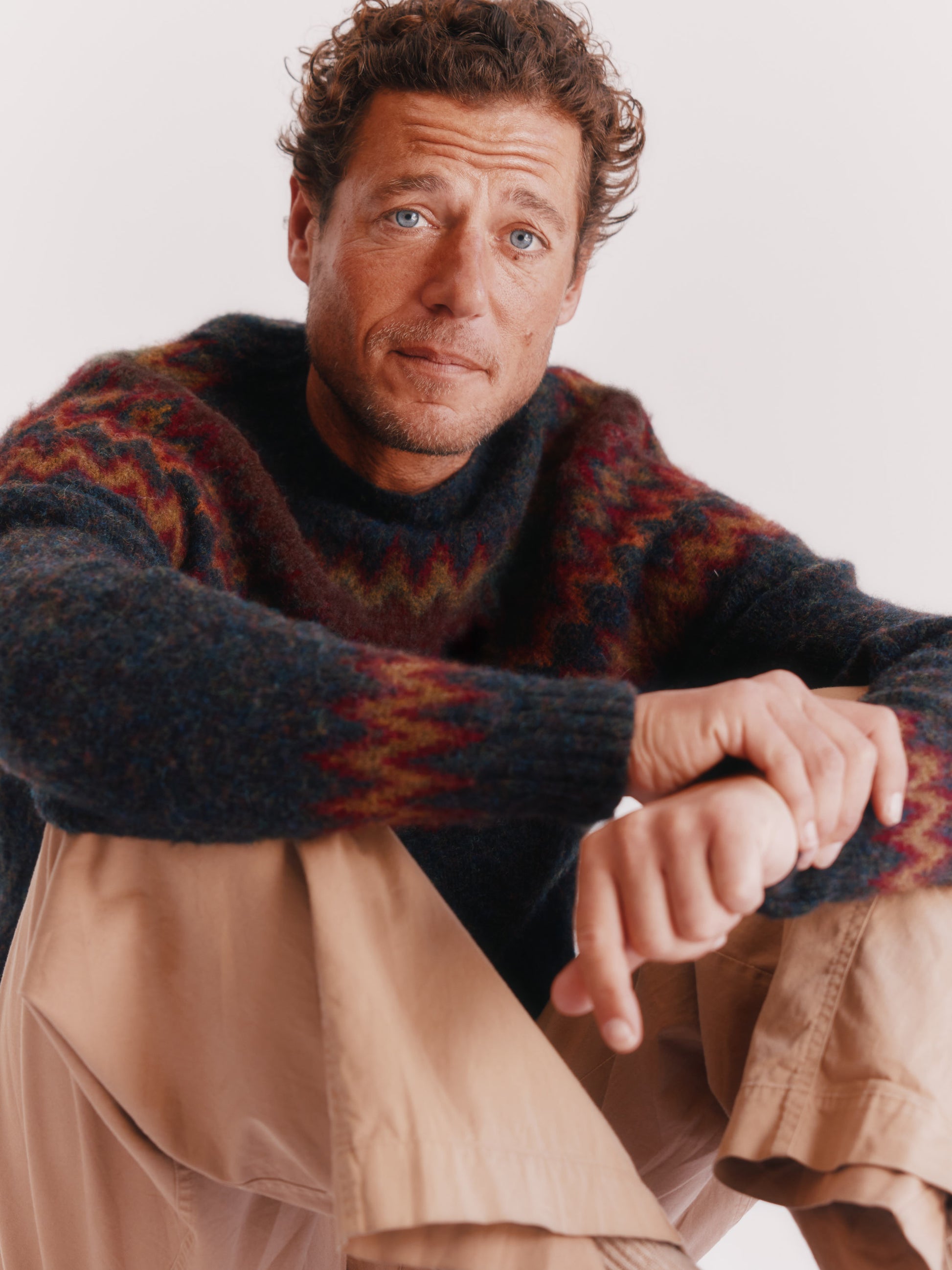 Man wearing a Bosie Fjord Nordic patterned sweater and beige pants on a white background